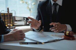 Lawyer gesturing with hands while discussing contract details with client in office, surrounded by legal documents and a gavel resting on the desk, facilitating clear communication