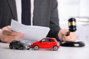 Auto accident law. Man with document and gavel at table indoors, focus on toy cars.