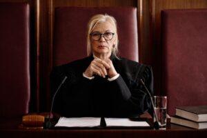 Mature impartial female judge in eyeglasses and black mantle looking at camera.