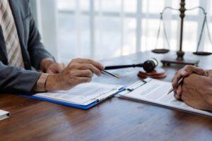 Close up of lawyers hands pointing at contract and insurance documents during a meeting, with gavel and scales of justice in background